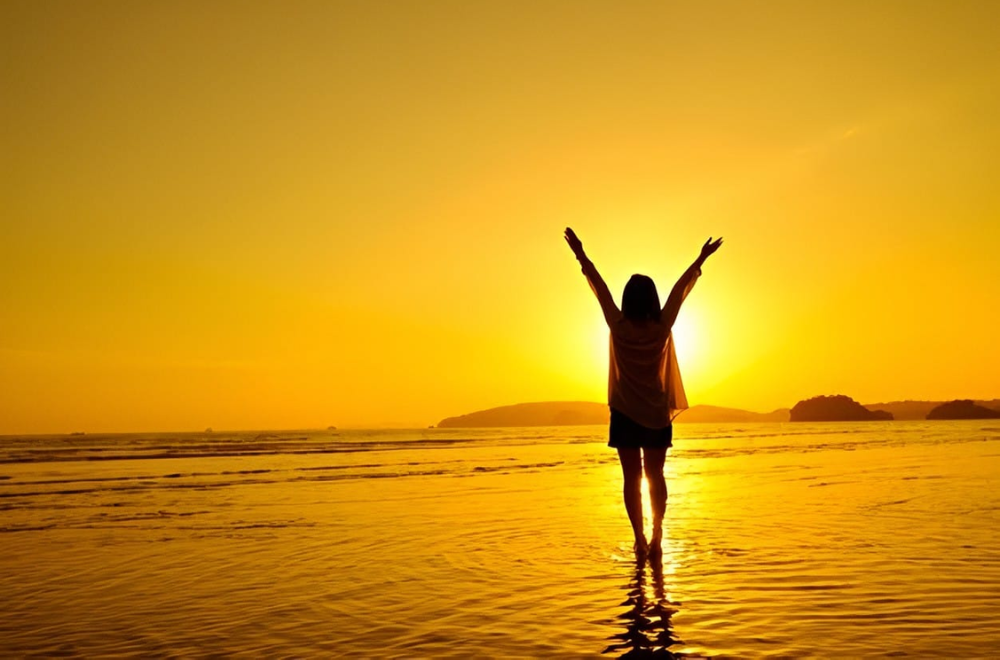 Il Valore del Tempo: Una persona che alza le braccia verso il cielo al tramonto sulla spiaggia, simbolo di libertà e riflessione sul tempo prezioso.