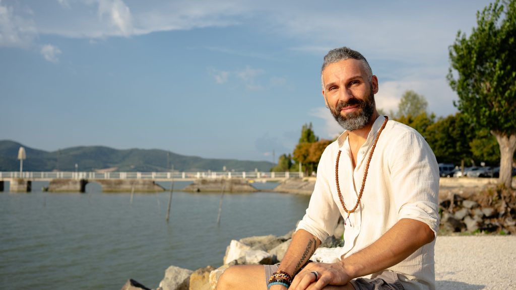 Luca, seduto vicino a un lago al tramonto, simbolo di serenità e introspezione, nel percorso per trasformare il caos in chiarezza.