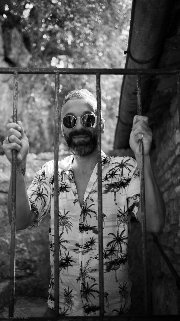 Luca, esperto di numerologia personale sorridente, dietro un cancello, simbolo di liberazione dai pesi del passato per vivere una vita nella piena sovranità, in un'atmosfera di calma e riflessione.